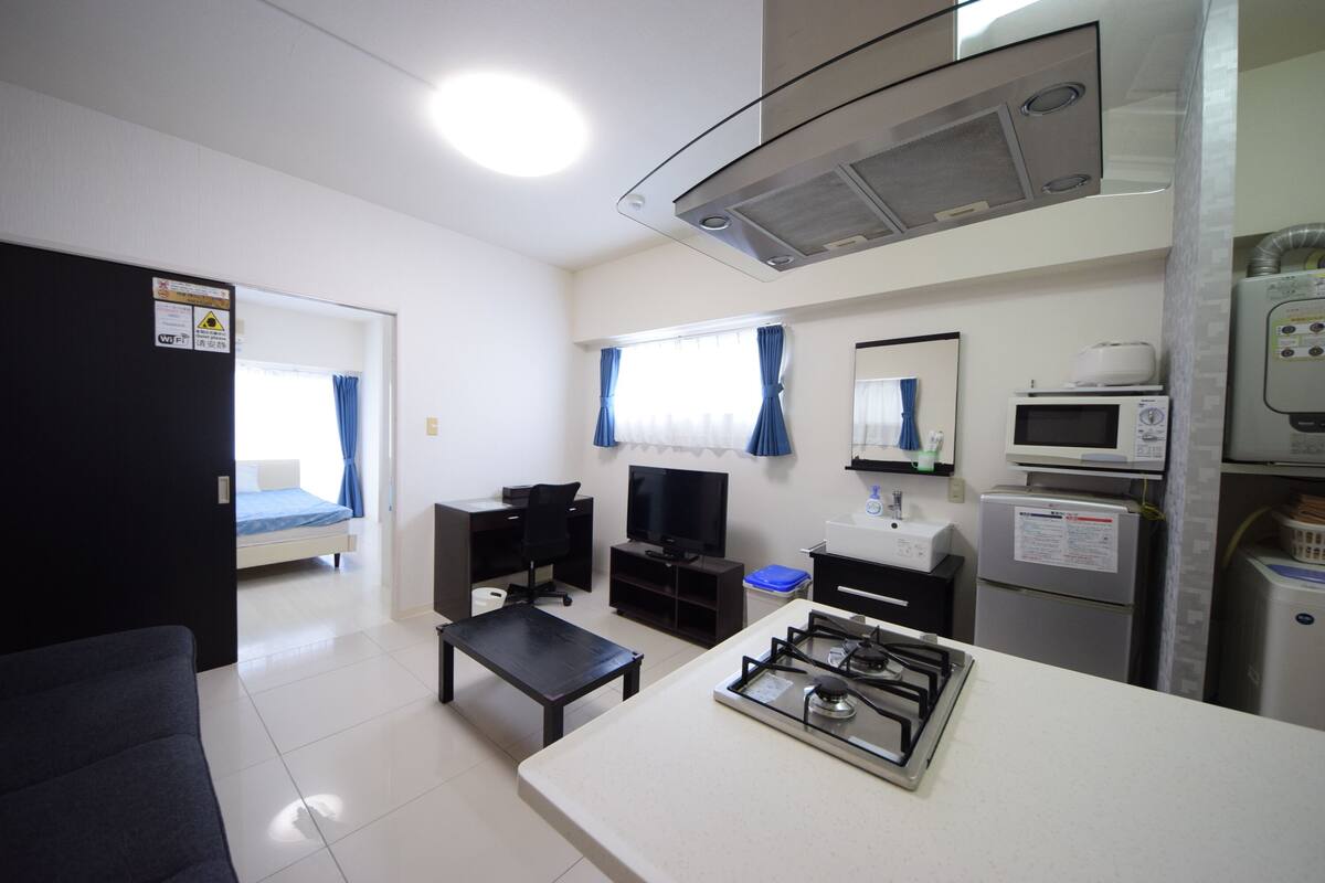 Een kleine hotelkamer met een kitchenette, een bed, een televisie en een eethoekje.