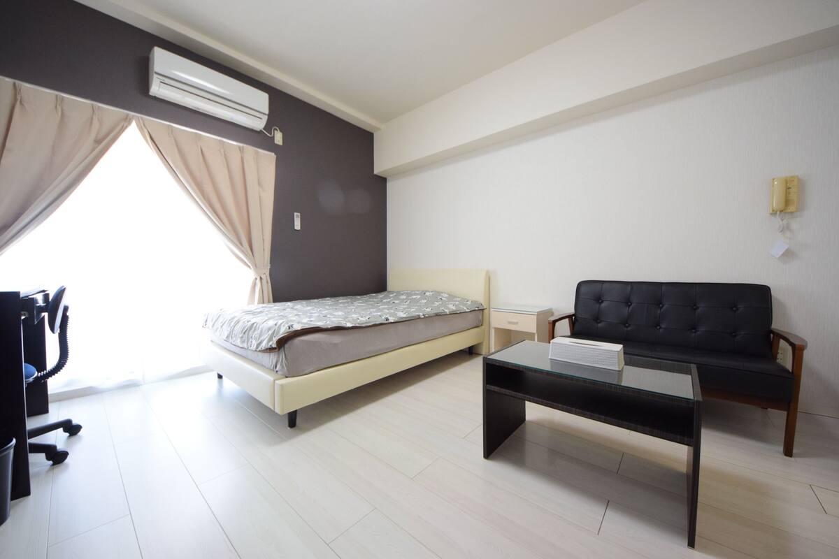 Een moderne slaapkamer met een bed, een zwarte bank, een glazen salontafel en een airconditioner.