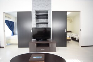 Una sala de estar moderna con un televisor de pantalla plana sobre un mueble de madera oscura, una pequeña mesa de centro y una estantería empotrada.