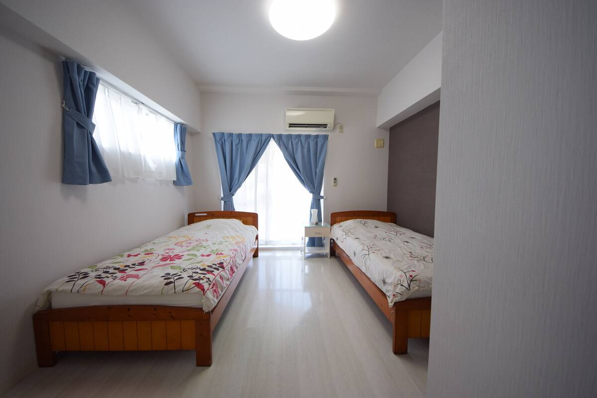 Een kamer met twee houten bedden, een witte airconditioning en een raam met blauwe gordijnen.