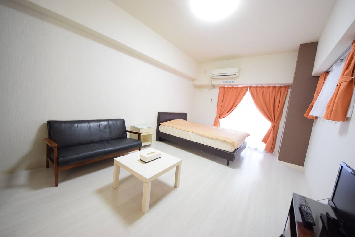 Een moderne hotelkamer met een zwarte leren bank, een enkel bed, een klein houten tafeltje en een televisie.