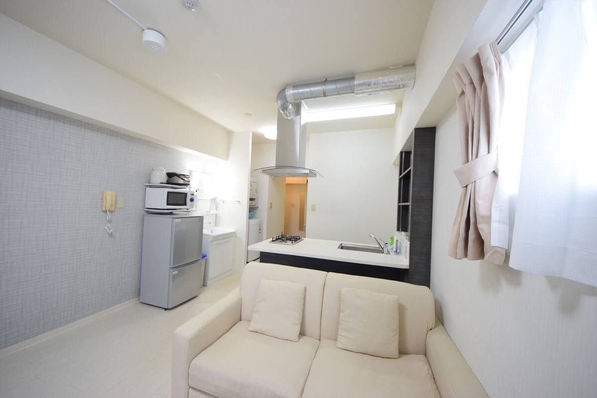 Een compacte leefruimte met een kitchenette, een slaapbank en een raam met gordijnen.