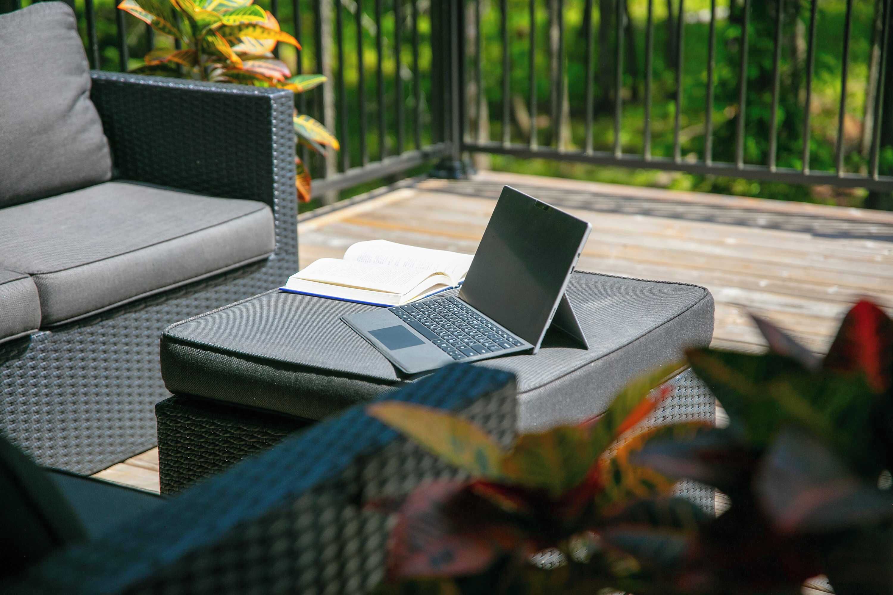 Een terras met een bank, een laptop op een standaard en een boek.