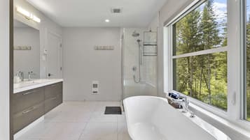 Une salle de bain moderne dotée d’une grande baignoire, d’une douche à l’italienne et d’une grande fenêtre donnant sur la verdure.