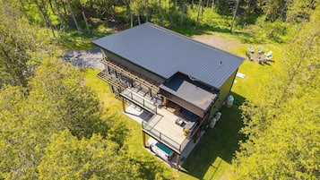 Une maison moderne à deux étages dotée d’une terrasse, d’une piscine et d’un grand jardin entouré d’arbres.