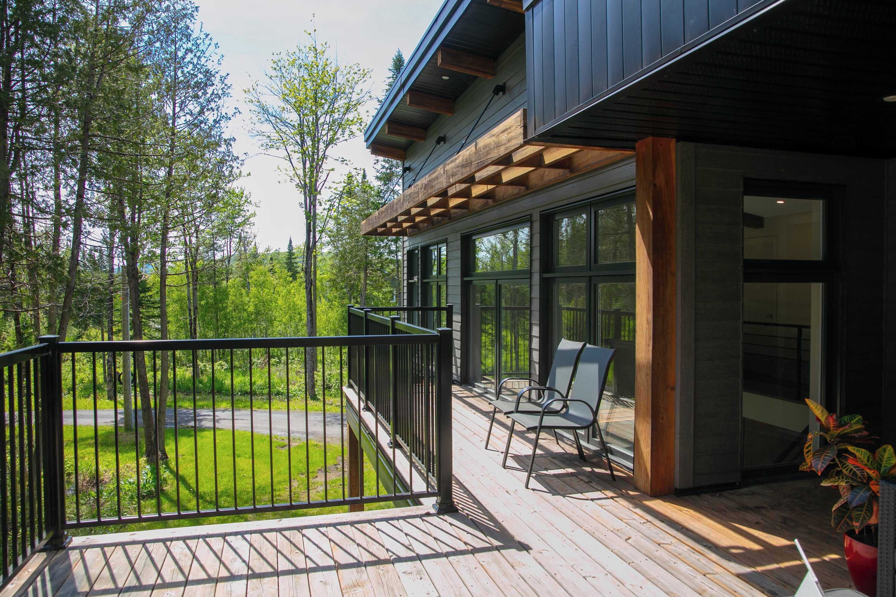 A wooden deck with a railing, a seating area with chairs, and a view of a forested area.