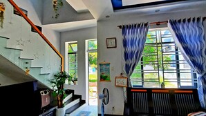 Une pièce avec un escalier, un radiateur, un ventilateur et une fenêtre avec des rideaux.