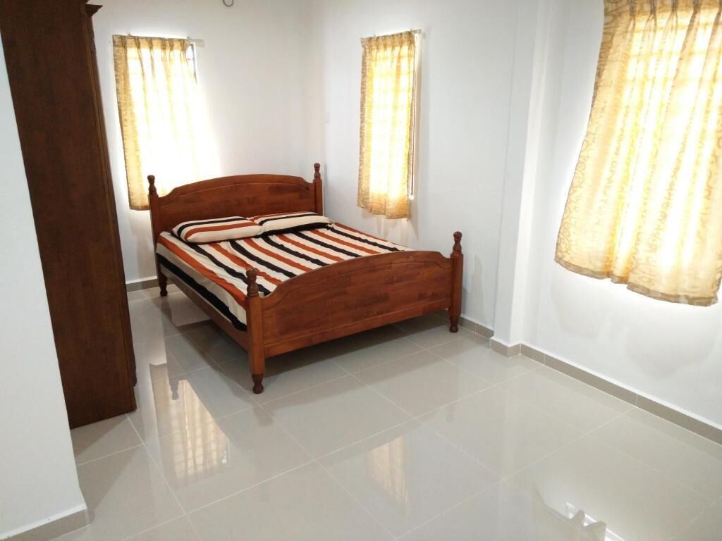 A bedroom with a wooden bed, two windows with curtains, and a tiled floor.