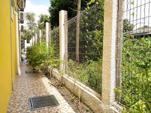 A narrow alleyway with a tiled floor, a metal fence, and greenery. - Harum Manis Country House (Kangar)
