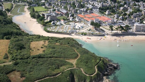 Oversigtsbillede af en kystby med en sandstrand, en lysthavn og parcelhuse.