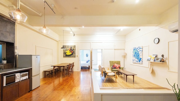 A spacious living area with a wooden floor, a dining table, and a seating area with a bench. - Pineapple Hotel (Naha)