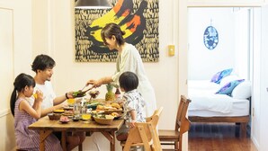A dining table with food and drinks, a bed with pillows, and a colorful abstract painting on the wall. - Pineapple Hotel (Naha)