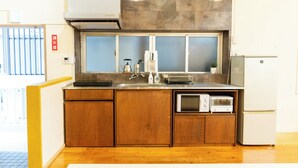 A compact kitchen with wooden cabinets, a built-in microwave, and a refrigerator. - Pineapple Hotel (Naha)