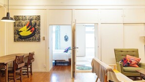 A room with a wooden dining table, chairs, a green armchair, and a bed with a colorful pillow. - Pineapple Hotel (Naha)