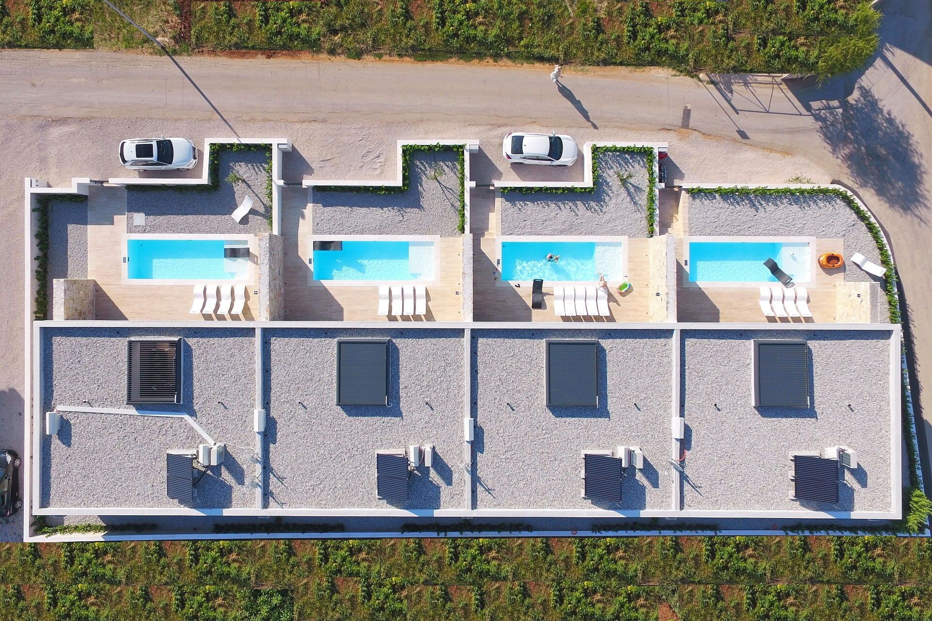 A rooftop with three swimming pools, each with lounge chairs and a person swimming.