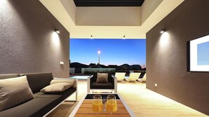 A modern living room with a sofa, a coffee table with drinks, and a view of the outdoors at dusk. - Villa Lea -  Home4You (Kraj)