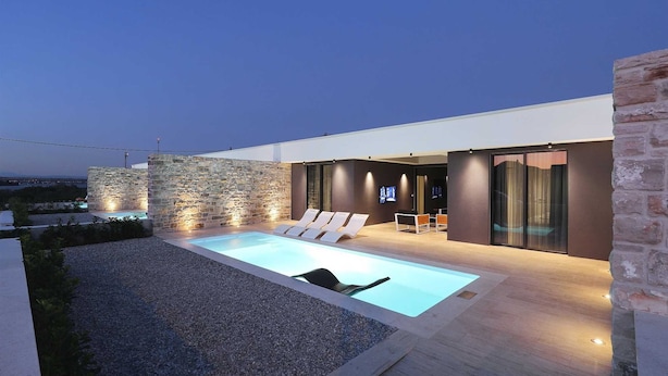 A modern outdoor pool area with stone walls and a lounge area with chairs and a table. - Villa Lea -  Home4You (Kraj)