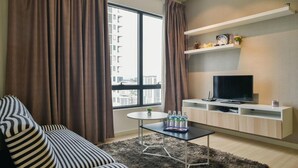 A modern living room with a sofa, a coffee table, a TV, and a window with curtains. - USJ One Premium Suites at Subang Sunway USJ (Subang Jaya)