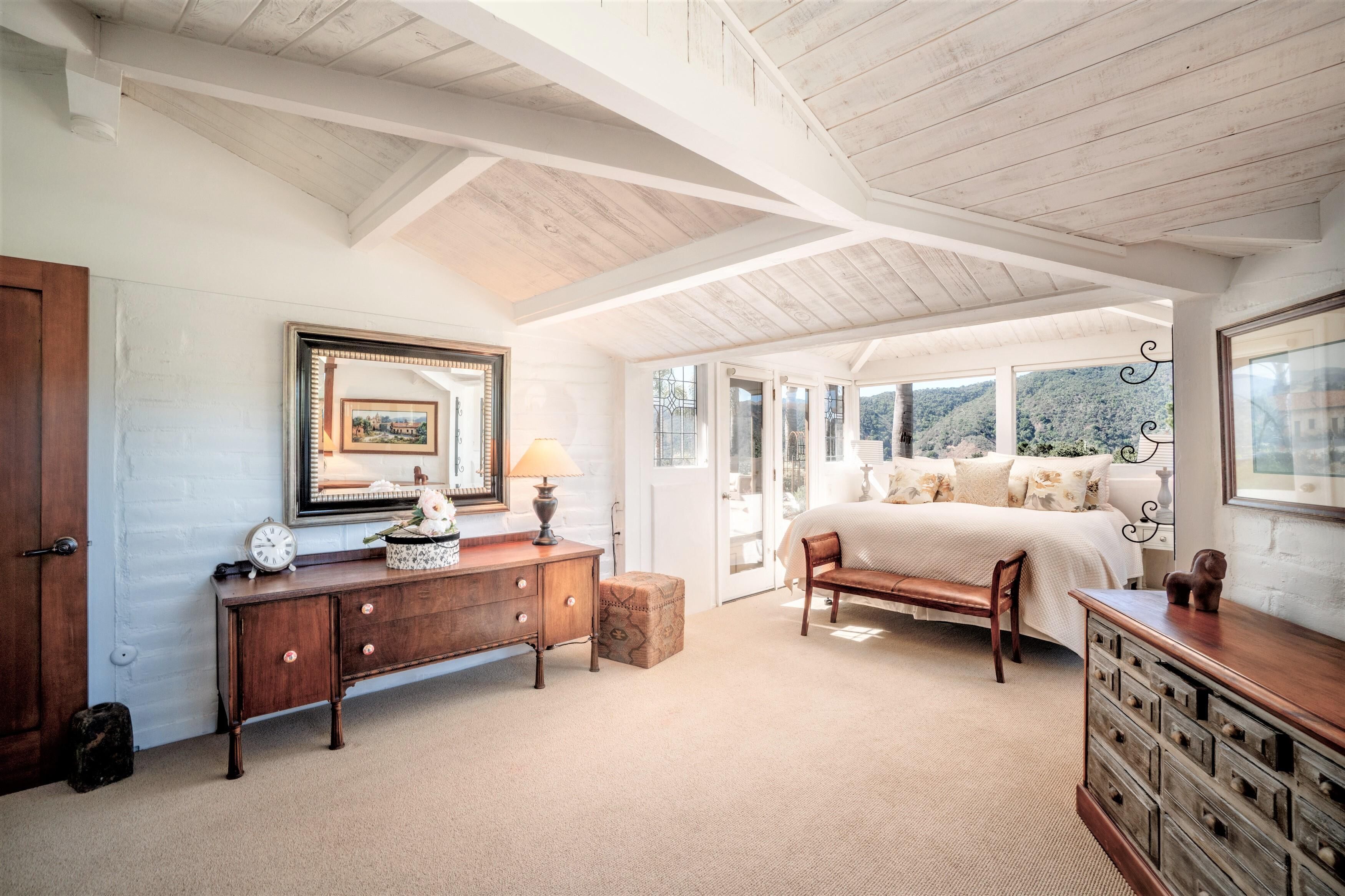 A bedroom with a large bed, wooden furniture, and a view of the outdoors.