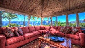 A red sectional sofa with patterned cushions, a wooden coffee table, and a view of mountains and trees through large windows. - Lx16: Valley View Estate Above The Wineries With Hot Tub (Carmel Valley)