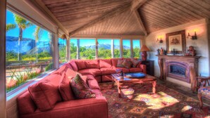 A cozy living room with a large red sectional sofa, a fireplace, and a view of a mountainous landscape through large windows. - Lx16: Valley View Estate Above The Wineries With Hot Tub (Carmel Valley)