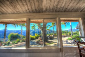Una habitación con amplios ventanales que dan a un jardín ajardinado y montañas.