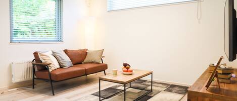 Ein Wohnzimmer mit einem braunen Ledersofa, einem Holztisch und einem Fernseher auf einem Holzständer.