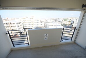 A balcony with a metal railing, a small decorative item, and a view of a cityscape with multiple buildings. - SUMUKA Shintoshin II (Naha)