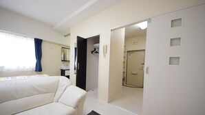 A modern hotel room with a sofa, a wardrobe, and a bathroom visible through an open door. - SUMUKA Shintoshin II (Naha)