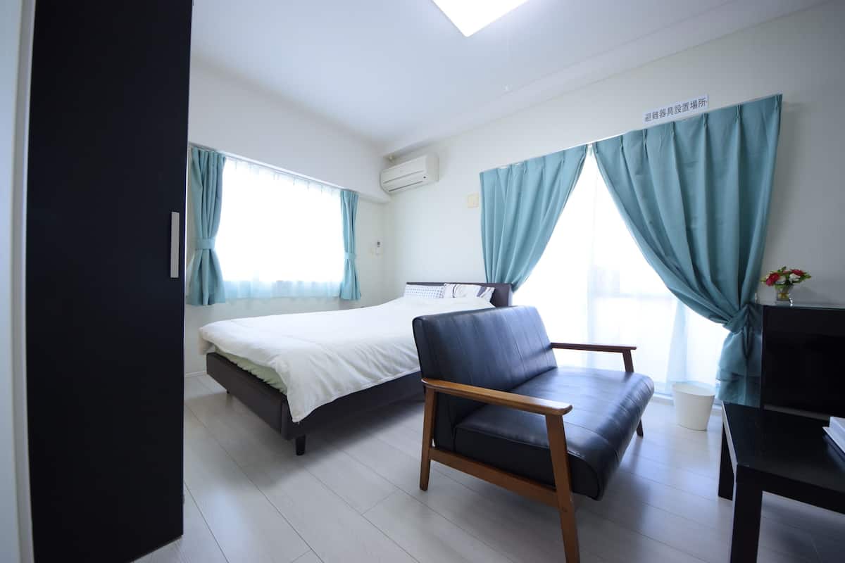 A hotel room with a bed, a chair, a desk, and a window with curtains.