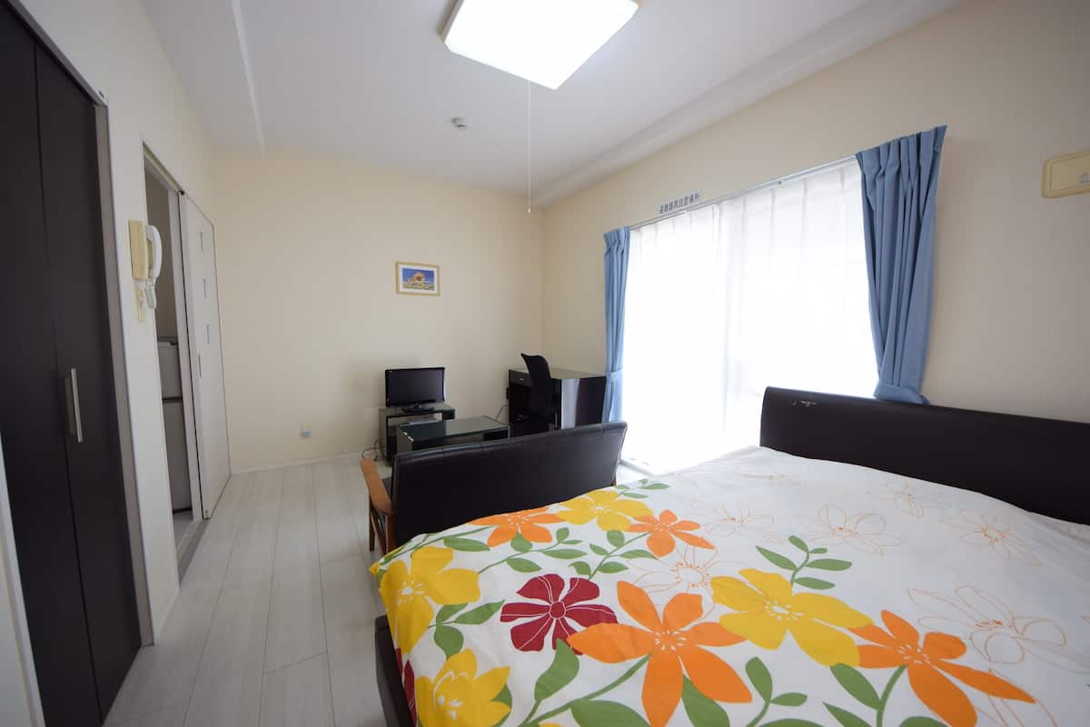 A hotel room with a bed, a desk, a chair, a television, and a window with curtains.