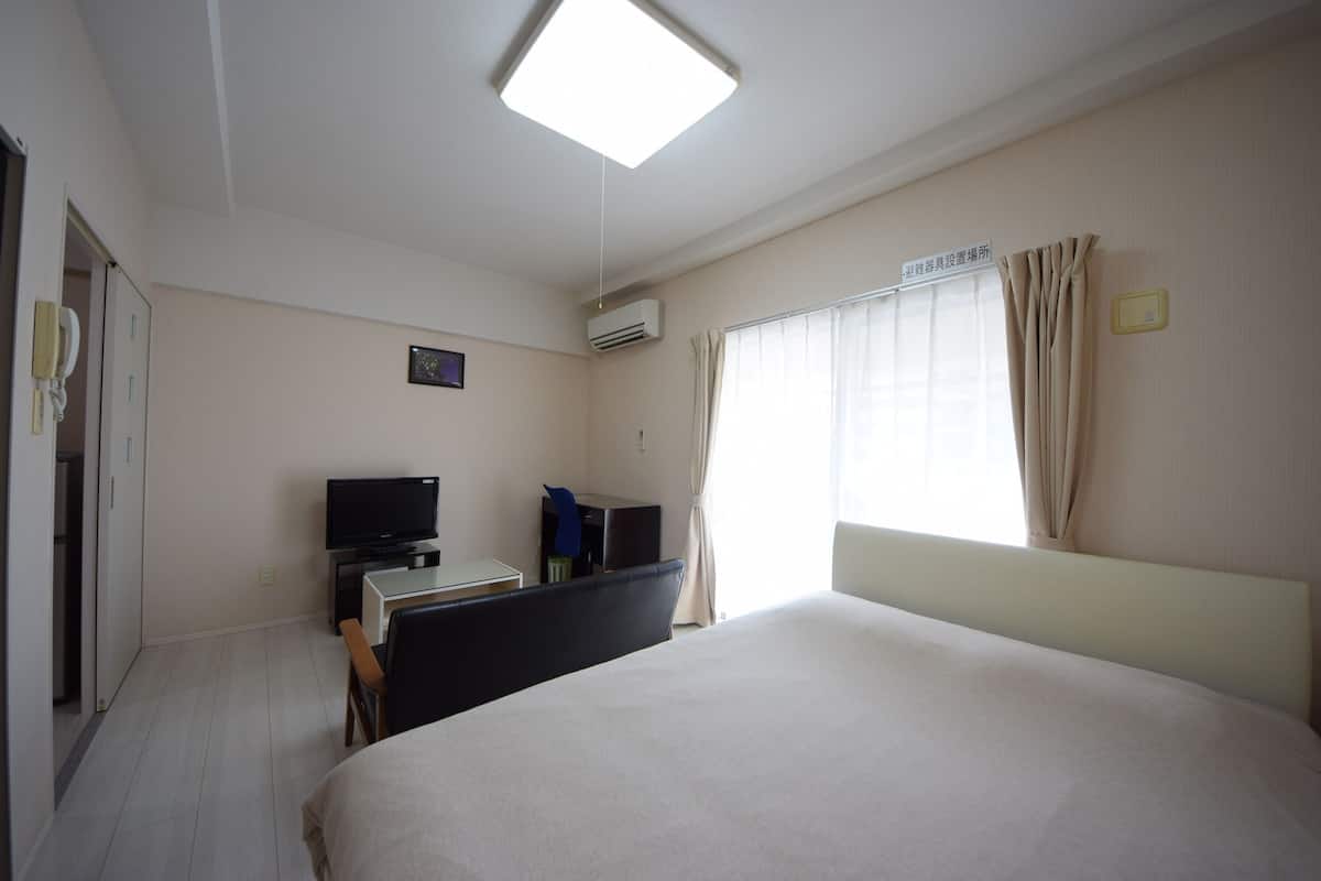 A hotel room with a bed, a desk with a computer, a television, and a window with curtains.