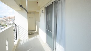 A balcony with a view of the city, a sliding glass door, and a white wall. - SUMUKA Shintoshin II (Naha)