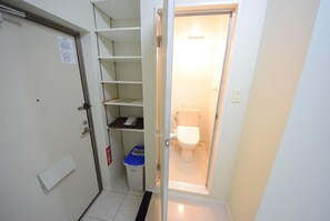 A compact bathroom with a toilet, a small shelf unit, and a trash bin. - SUMUKA Shintoshin II (Naha)