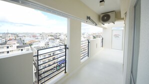 A balcony with a city view, a ceiling fan, and a door. - SUMUKA Shintoshin II (Naha)