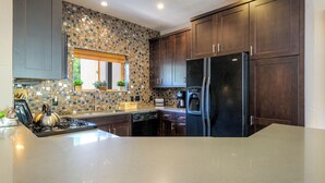 Une cuisine moderne avec des meubles de rangement en bois foncé, un réfrigérateur noir et un pare-feu en carreaux.