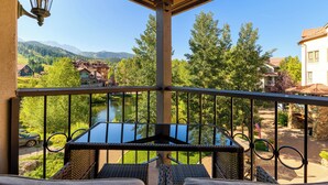 Un balcon avec une table et des chaises donnant sur un paysage pittoresque, avec une rivière, des arbres et des montagnes en toile de fond.
