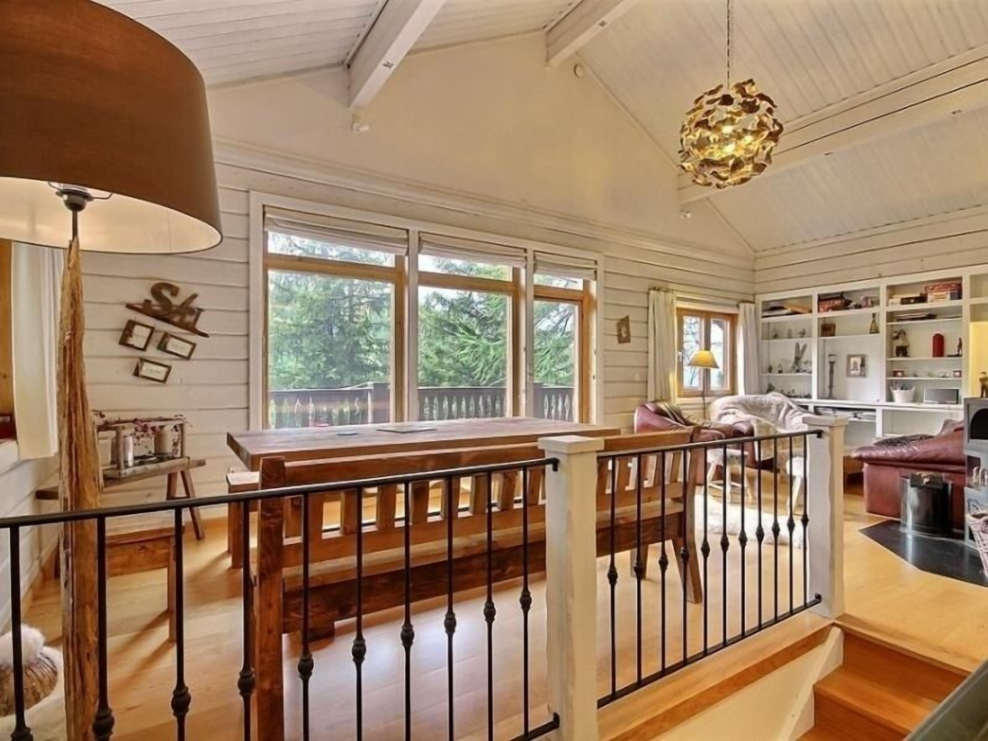 A spacious living area with a wooden staircase, large windows, and a cozy seating area.