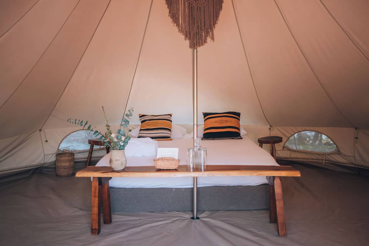 A tent with a bed, a wooden table, and a hanging light fixture.