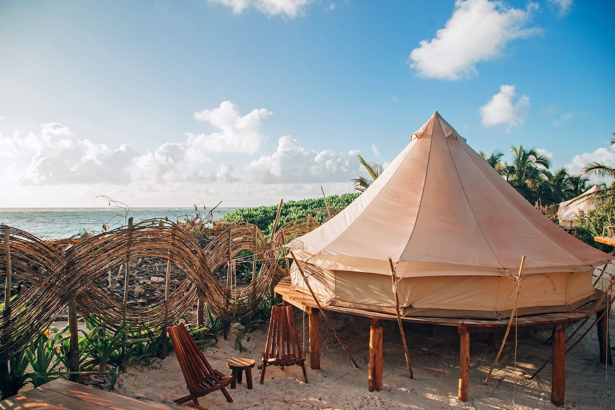 A beach tent with a view of the ocean, surrounded by palm trees and wicker furniture.