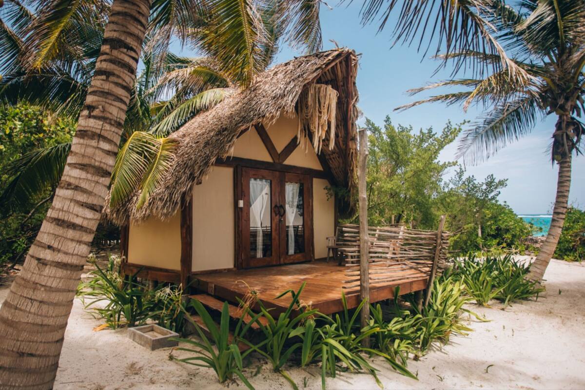 A beach house with a thatched roof, wooden deck, and a view of the ocean.