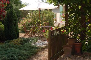 Une terrasse de jardin avec une table et des chaises en bois, entourée de plantes en pot et d’une clôture en bois.