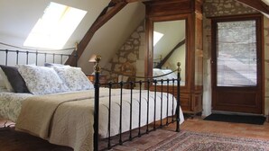 Ein Schlafzimmer mit schrägen Wänden, einem Bett mit Metallgestell, einer Chandelüster und einer Steinwand.