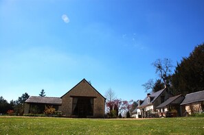 Un bâtiment en pierre doté d’un toit triangulaire, entouré d’une zone herbeuse et d’arbres.