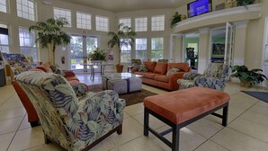 A spacious living area with a large sofa, armchairs, and a coffee table. There are several potted plants and a television mounted on the wall. - Wyndham Palms (Kissimmee)