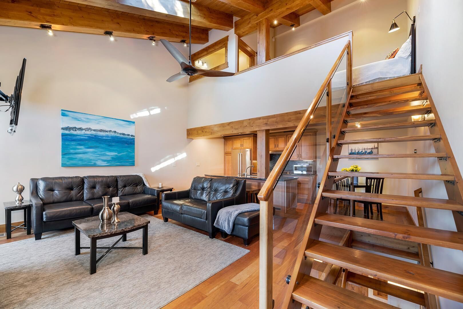 A spacious living area with a modern design, featuring leather sofas, a wooden staircase, and a large painting on the wall.
