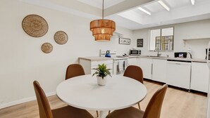 A modern kitchen with white cabinets, a round dining table with brown chairs, and a hanging rattan light fixture.