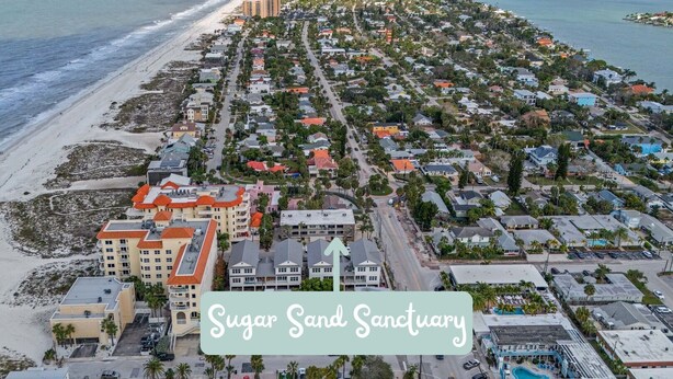 An aerial view of Sugar Sand Sanctuary with beachfront properties, a central road, and a swimming pool area.