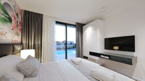 A modern hotel room with a large bed, a flat-screen TV, a built-in desk, and a view of a swimming pool. - Villa Lana - Home4You (Kraj)