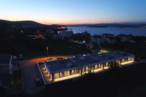 Un edificio moderno con techo plano, rodeado de un estacionamiento y un cuerpo de agua al fondo.